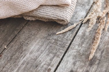 Sonbahar ya da kış geçmişi. Bir yığın yün kazak ve ahşap masada kurutulmuş bitki. Hygge havası, soğuk hava konsepti. El yapımı örgü kazaklar.
