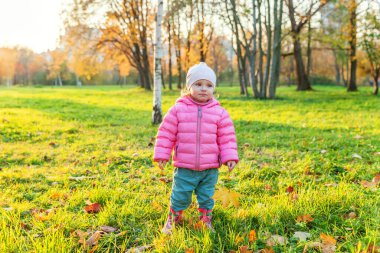 Güzel sonbahar parkında, doğa yürüyüşlerinde gülümseyen mutlu genç kız. Sonbaharda düşen sarı akçaağaç yaprağıyla oynayan küçük bir çocuk turuncu arka planda düşer. Merhaba sonbahar konsepti