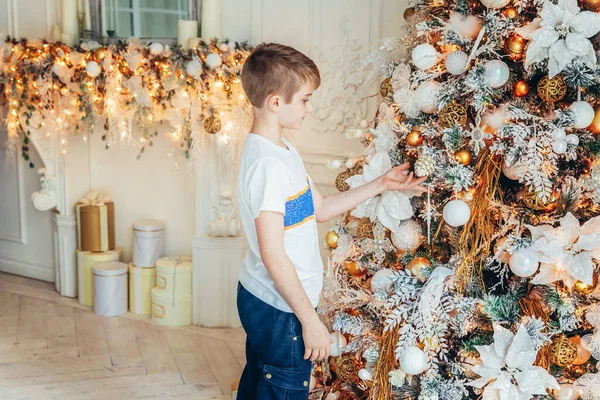 Jonge jongen versiert kerstboom op kerstavond thuis. Jonge jongen in lichte slaapkamer met winterdecoratie. Gelukkig gezin thuis. Kerstmis Nieuwjaar december tijd voor viering concept — Stockfoto