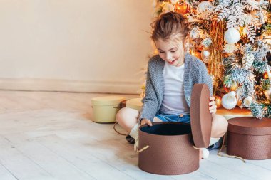 Noel arifesinde Noel ağacının yanında hediye kutusu olan küçük bir kız. Küçük çocuk kış dekorasyonlu, açık renk yatak odasında. Noel Yeni Yıl Kutlama Konsepti Zamanı