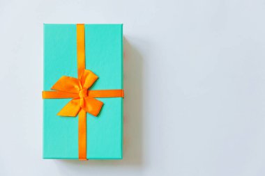 Noel yeni yıl sevgililer günü kutlaması. Romantik bir hediye. Minimum tasarım mavi hediye kutusu. Beyaz arka planda turuncu kurdele var. Düz görünüm kopyalama alanı