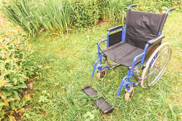 Empty wheelchair standing on grass in hospital park waiting for patient services. Invalid chair for disabled people parked outdoor in nature. Handicap accessible symbol. Health care medical concept