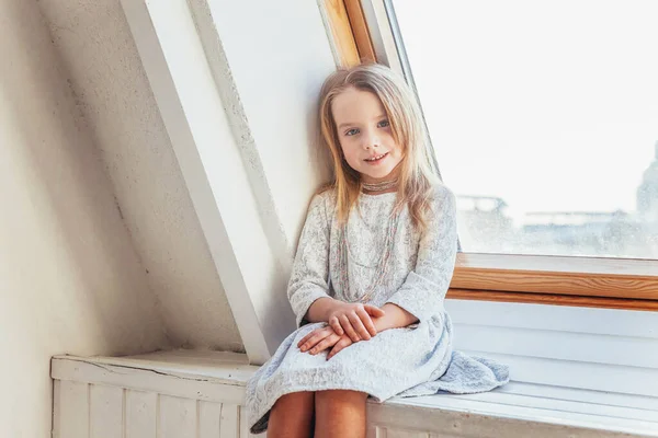 白いドレスの小さなかわいい甘い笑顔の女の子が窓の上に座って 屋内で明るい光のリビングルームにあります 子供の頃の若者のリラックスコンセプト — ストック写真