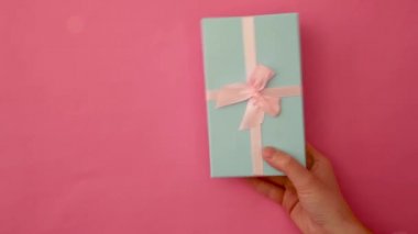 Pembe renkli arka planda izole edilmiş mavi hediye kutusunu tutan kadın eli tasarımı. Noel yeni yıl sevgililer günü kutlaması. Romantik bir hediye. Boşluğu kopyala