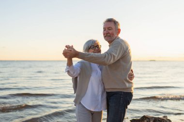 Yürümeye devam. Romantik olgun çift plaj gezisinde birlikte dans ediyor. Mutlu gülümseyen aile emeklisi kadın koca eş birlikte eğleniyor. Aile zamanı aşk bakımı