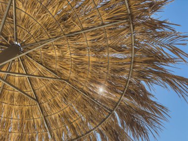 Güneş ışınlı saman şemsiyesi. Sıcak yaz gününde kumsalda saman şemsiyesi. Güneşli mavi gökyüzü samandan yapılmış güneş şemsiyesi altında sıcak havanın tadını çıkarıyor. Tropikal ülkelerde tatil