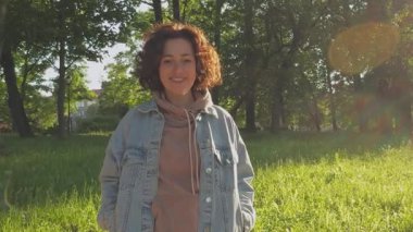 Şehir parkında gün batımında gülümseyen güzel bir genç kadın. Gülümseyen genç bir kızın açık hava portresi. Kadınlar güneşli yaz günlerini dışarıda dinlenerek geçiriyorlar. Özgürlük mutluluğu kaygısız mutlu insanlar