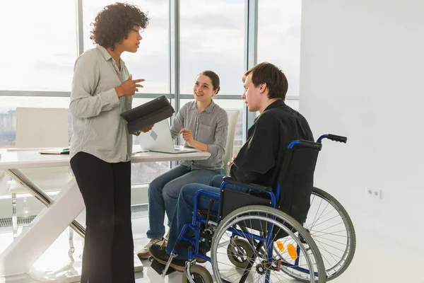 Takım çalışması beyin fırtınası. Çeşitli çok ırklı meslektaşlar birlikte çalışan engelli insanlar için sandalyede oturuyor. Yaratıcı ofiste oturup iş konuşan bir grup insan. Genç profesyonel takım