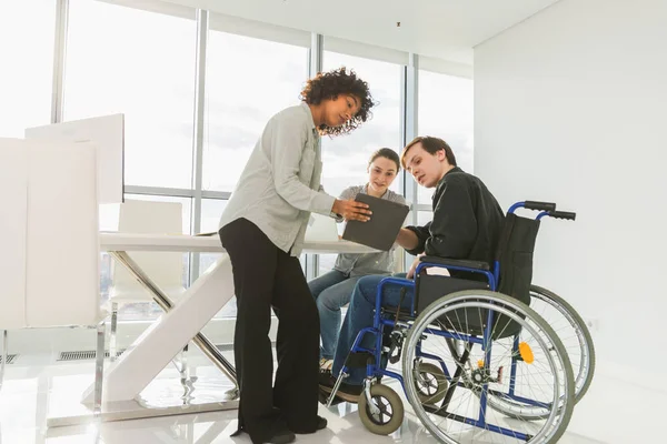 Takım çalışması beyin fırtınası. Çeşitli çok ırklı meslektaşlar birlikte çalışan engelli insanlar için sandalyede oturuyor. Yaratıcı ofiste oturup iş konuşan bir grup insan. Genç profesyonel takım