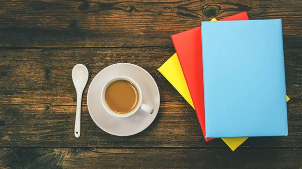 white cup of coffee and books in colored covers. flat view. wooden background