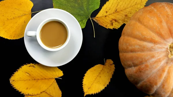 a cup of coffee, pumpkin and autumn leaves on a dark background.