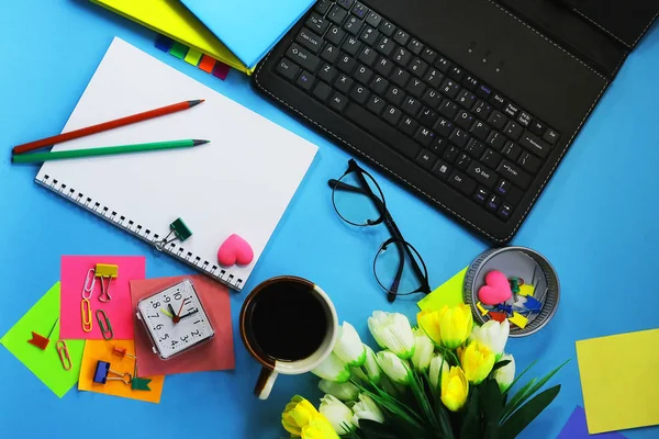 office workspace. Clock. artificial flowers, coffee, stationery, glasses, keyboard. toned background