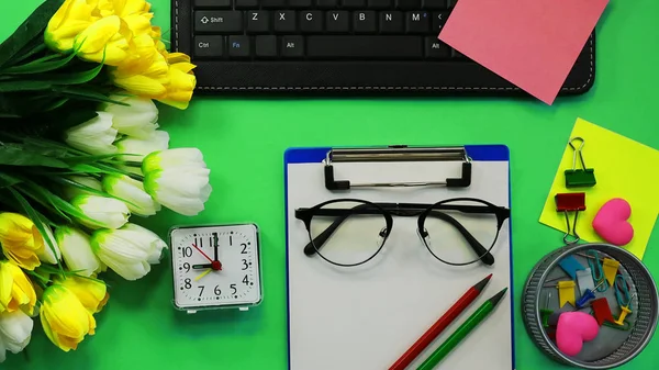 office workspace. Clock. artificial flowers, stationery, glasses, keyboard. toned background
