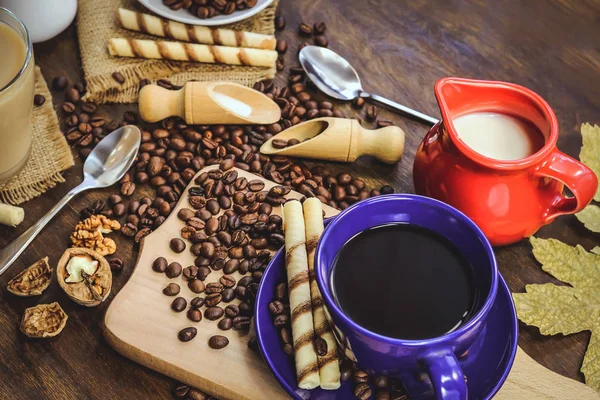 a cup of coffee and a jug of milk. coffee beans. wooden background.