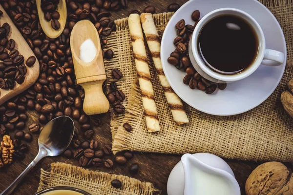 a cup of coffee and a jug of milk. coffee beans. wooden background.