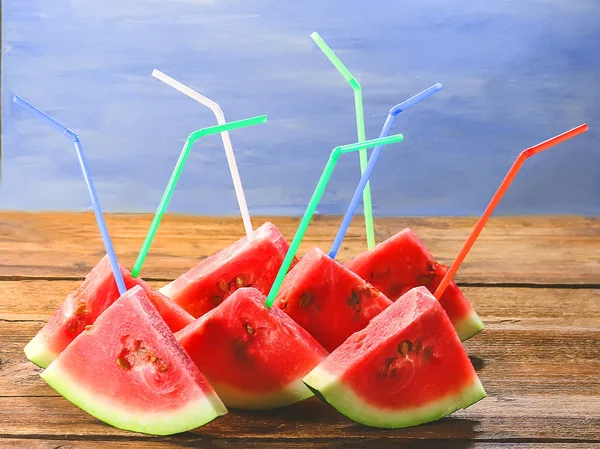 slices of watermelon with straws for juice. on a wooden and blue background.