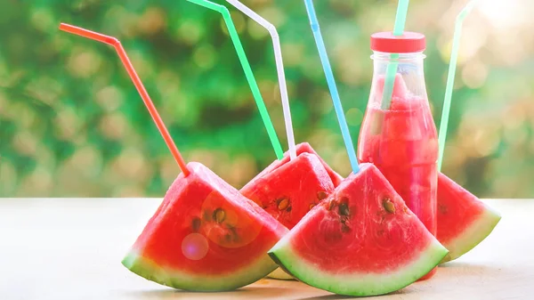 Slices of watermelon with straws for juice.  Bottles with juice and slices.