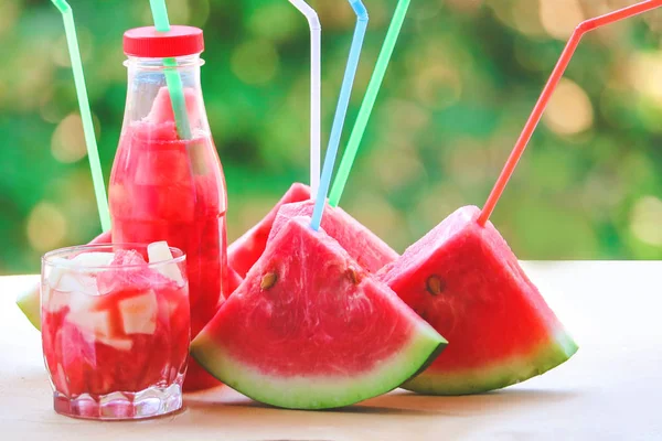 Slices of watermelon with straws for juice.  Bottles with juice and slices.