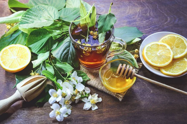 lime tea, lemon, flowers and honey in a glass bowl. on a wooden background.
