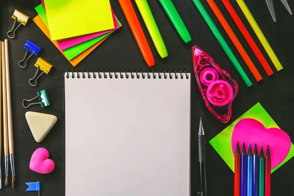 School and office stationery on a background of a dark wooden board.