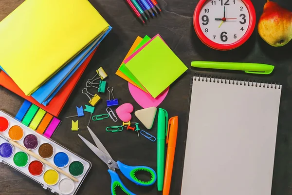 School and office stationery on a background of a dark wooden board.