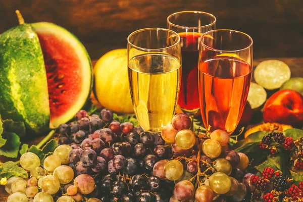 glasses with pink, white and red wine. grapes and other fruits on a wooden background.