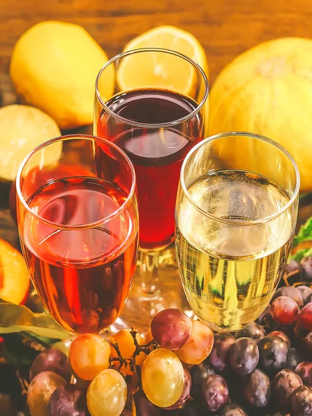 glasses with pink, white and red wine. grapes and other fruits on a wooden background.