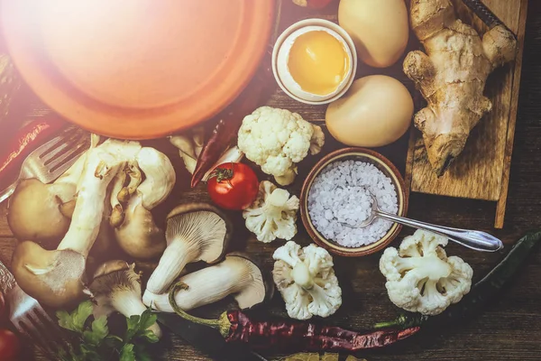 various food ingredients for cooking. mushrooms, chicken eggs, tomatoes. kitchen accessories. sunlight. wooden background.