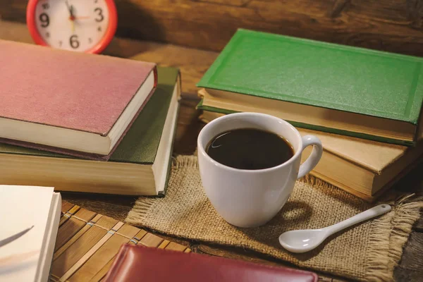 cup of coffee among books on a wooden table.