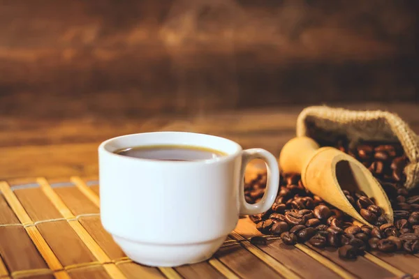 cup of black coffee and grains of coffee in a bag on a wooden table