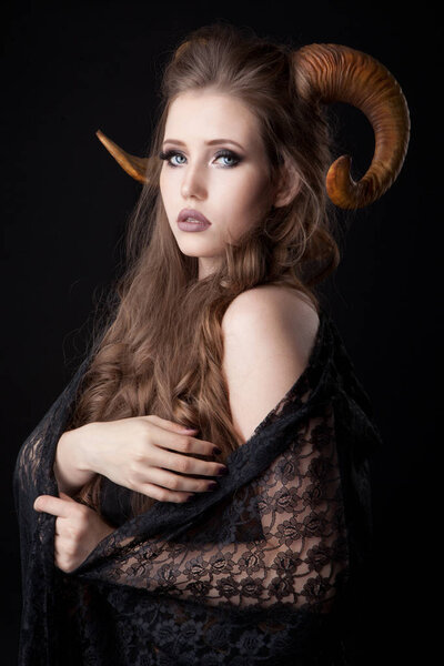 Portrait of an attractive demon woman with horns and curly hair, studio shot for Halloween