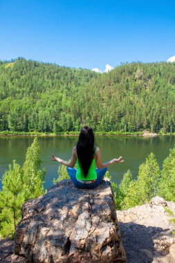 Kadın bir kayaya dağın zirvesinde yoga yaparken lotus duruş içinde meditasyon.