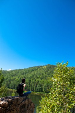 Dağ uçurumun tepesinde oturan genç seyahat kadın.