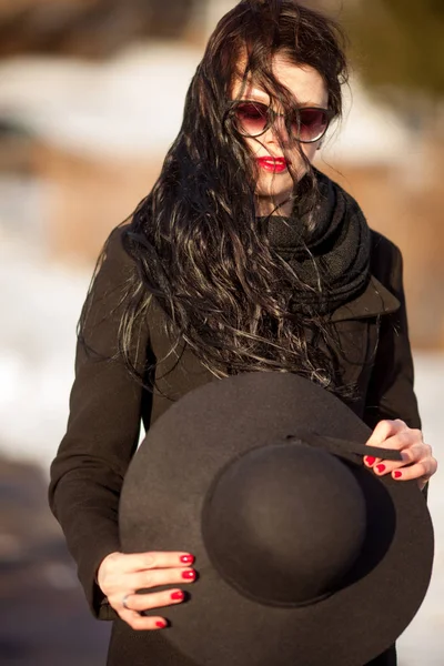 Junge Frau posiert in schwarzem Mantel und schwarzem Hut. — Stockfoto