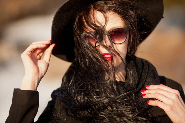 Молода жінка позує в чорному пальто і чорному капелюсі . — стокове фото