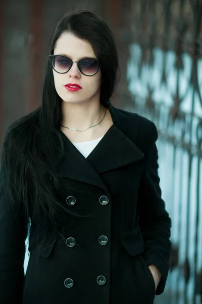 Young woman posing in black coat and black hat.