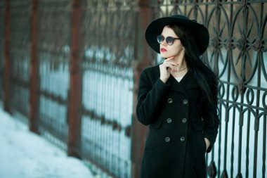 Genç kadın siyah ceket ve siyah şapka poz.