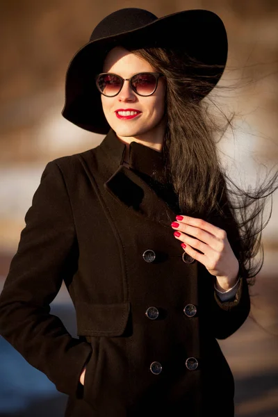 Νεαρή γυναίκα που παρουσιάζουν στο μαύρο παλτό και μαύρο καπέλο. — Φωτογραφία Αρχείου