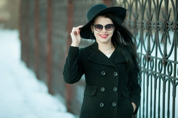 Fiatal nő fekete kabátot és fekete kalapban pózol. — Stock Fotó
