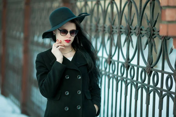 Giovane donna in posa in cappotto nero e cappello nero . — Foto Stock