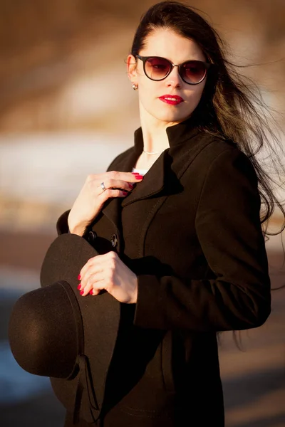 Jonge vrouw poseren in zwarte jas en zwarte hoed. — Stockfoto