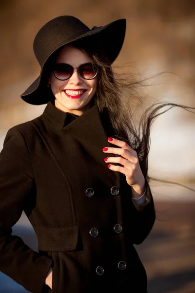 Νεαρή γυναίκα που παρουσιάζουν στο μαύρο παλτό και μαύρο καπέλο. — Φωτογραφία Αρχείου