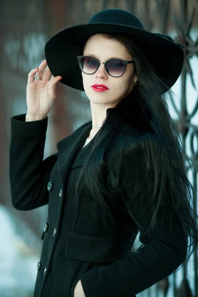 Fiatal nő fekete kabátot és fekete kalapban pózol. — Stock Fotó