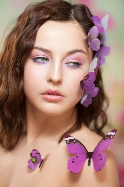 Schöne junge Frau mit künstlichem Schmetterling im lockigen Haar. — Stockfoto