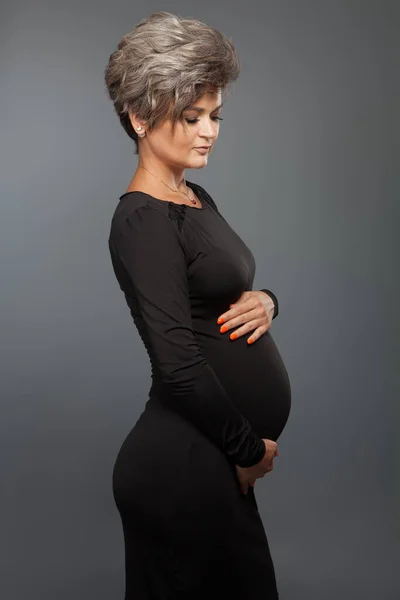 Портрет любящей беременной женщины, смотрящей на живот во время позирования — стоковое фото