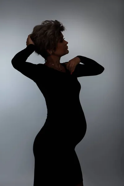 Силуэт любящей беременной женщины, смотрящей в камеру во время позирования — стоковое фото