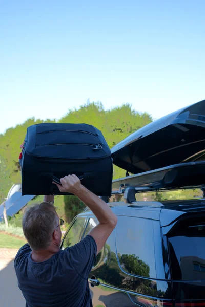 Man loading suitcase into roof box on top of car