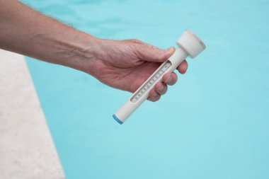 Yüzme havuzunun arka planında termometre tutan insanlar