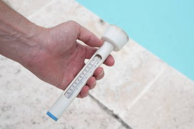 Yüzme havuzunun arka planında termometre tutan insanlar