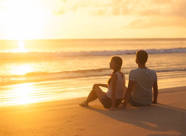 Silueta puesta de sol de pareja joven enamorada sentada en la playa —  Fotos de Stock